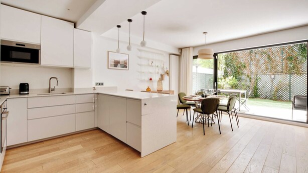 A modern kitchen with white cabinetry, a central island, and a dining area with a table and chairs. - Passy / Eiffel Tower - Amazing 2BR with garden (Paris)