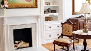 A room with a fireplace, a bookshelf, a chair, a table, and a mirror. - The Queen On Main (Winters)