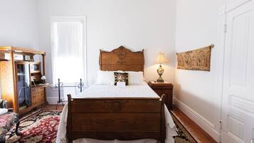 A bedroom with a wooden bed, a nightstand with a lamp, a dresser, and a large window.