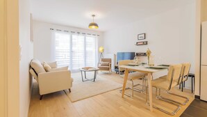 Una sala de estar moderna con un sofá, una mesa de comedor con sillas, una mesita auxiliar y una lámpara.