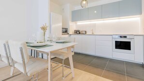 Una cocina moderna con armarios blancos, horno empotrado y comedor con mesa y sillas blancas.