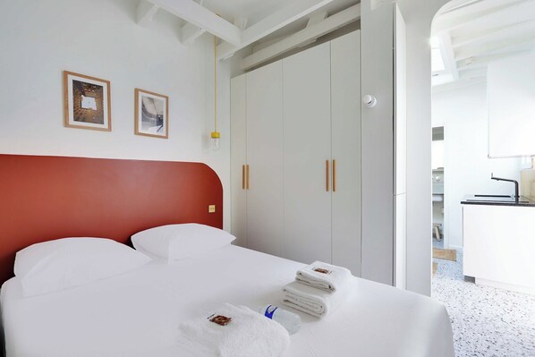 A hotel room with a red headboard, white bed, and a wardrobe with wooden handles. There are towels and a bottle on the bed. - Cosy apartment 2P close to Sacré-Coeur (Paris)