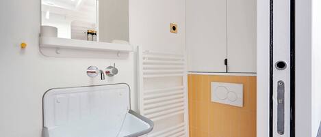 A bathroom with a white sink, a mirror, a towel rack, a radiator, and a door with a handle.