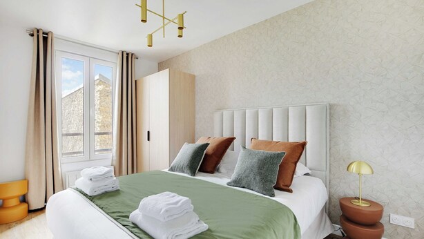 A neatly made bed with green and white bedding, a bedside lamp, and a window with curtains. - Cosy apartment -1BDR/3P - Ivry-sur-Seine (Ivry-sur-Seine)