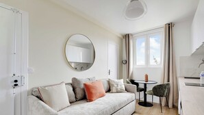 A modern living room with a sofa, a round mirror, a dining table with chairs, and a kitchen area. - Cosy apartment -1BDR/3P - Ivry-sur-Seine (Ivry-sur-Seine)