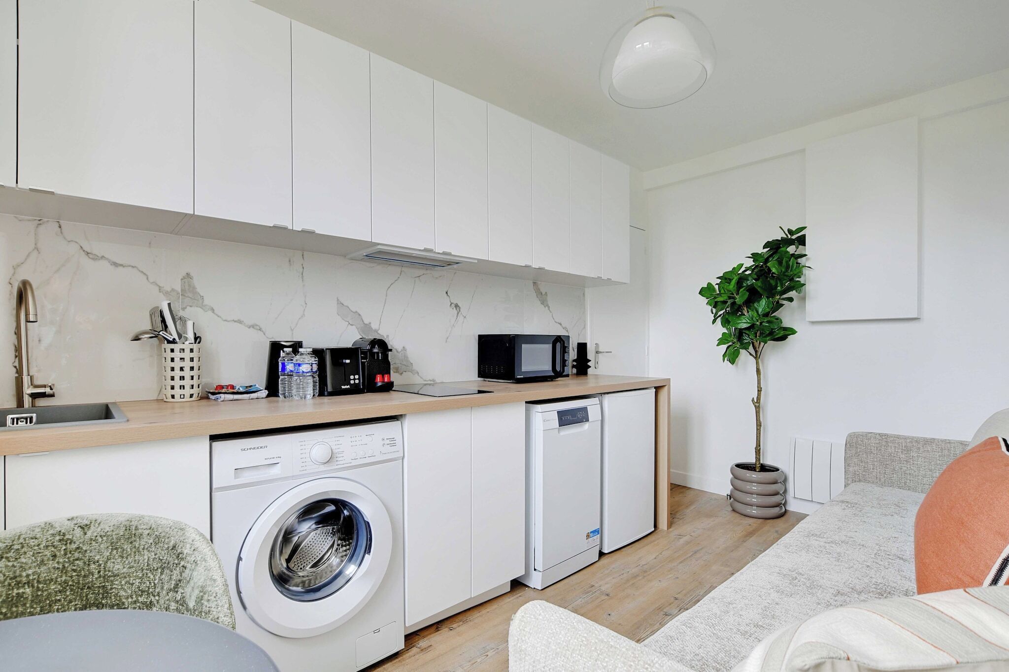A compact kitchen with white cabinets, a washing machine, a dishwasher, a microwave, and a sink.
