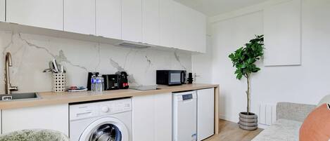 A compact kitchen with white cabinets, a washing machine, a dishwasher, a microwave, and a sink.