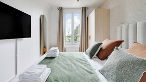 A neatly made bed with pillows, a flat-screen TV mounted on the wall, and a window with curtains. - Cosy apartment -1BDR/3P - Ivry-sur-Seine (Ivry-sur-Seine)