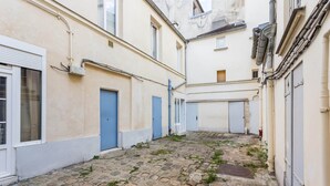 A narrow cobblestone alleyway between buildings with blue doors and a white window.