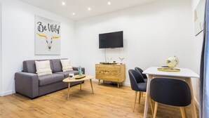 A modern living room with a grey sofa, a wooden cabinet, a small table, and a TV mounted on the wall.