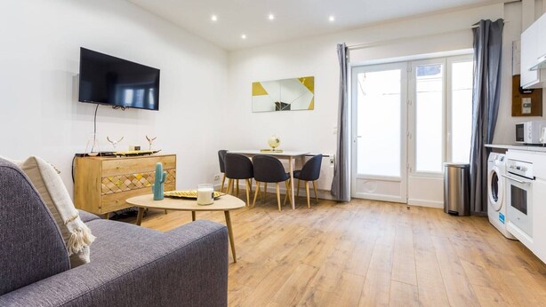 A modern living room with a flat-screen TV, a dining area, and a kitchen with a washing machine.