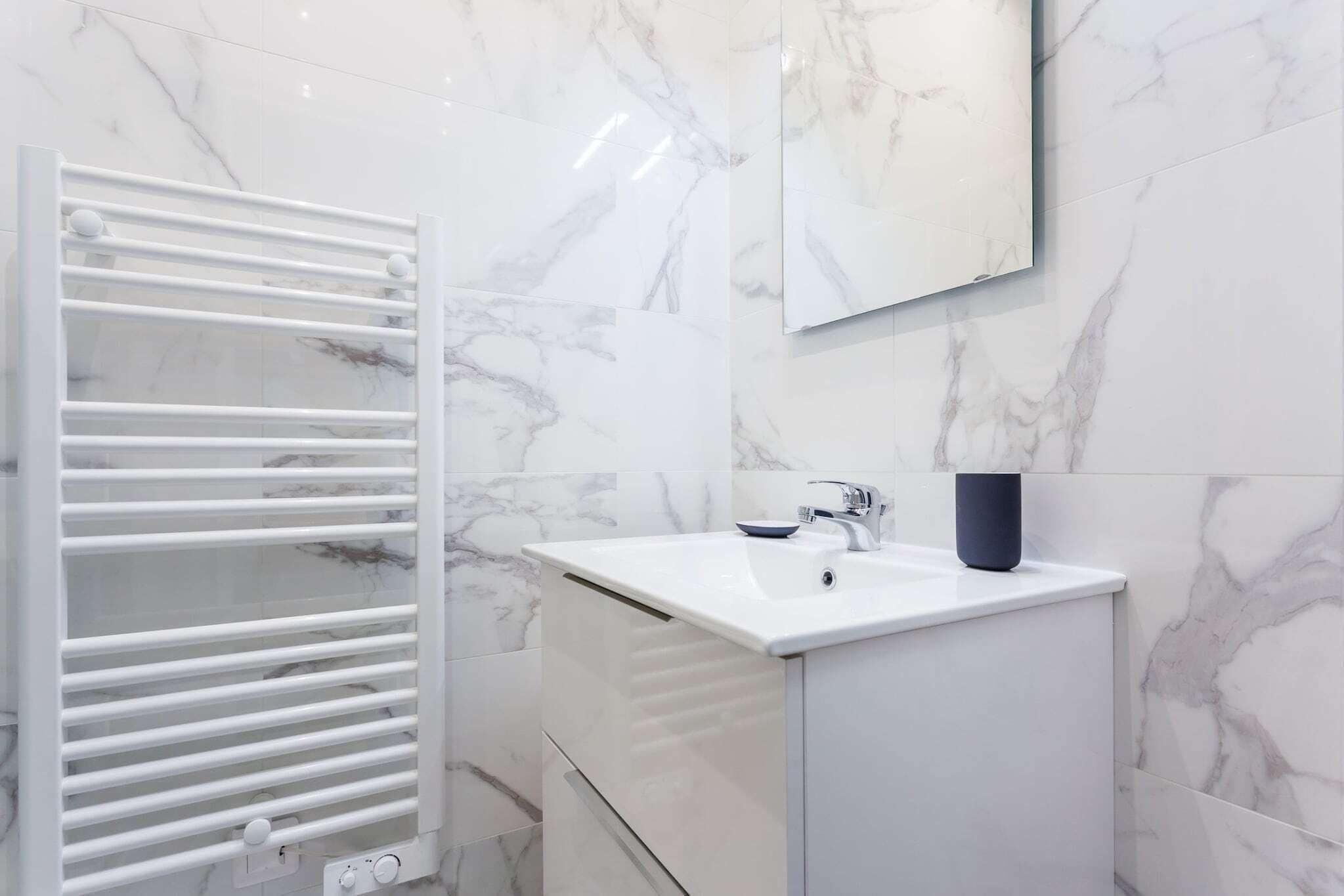 A bathroom with a white marble sink, a white towel rack, and a mirror above the sink.
