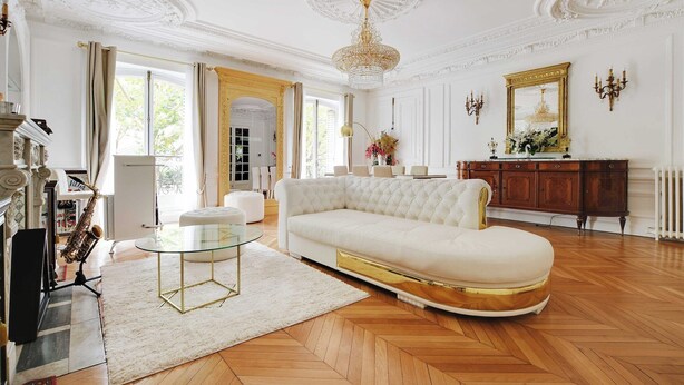 A spacious living room with a white sofa, a glass coffee table, and a chandelier.