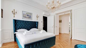 A bedroom with a large bed, white walls, a chandelier, and a wooden floor.