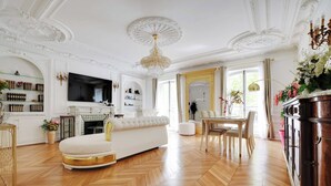 A spacious living room with a white sofa, a fireplace, a television, and a dining area with chairs.