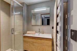 A modern bathroom with a glass shower enclosure, a wooden vanity, a large mirror, and a built-in heater.