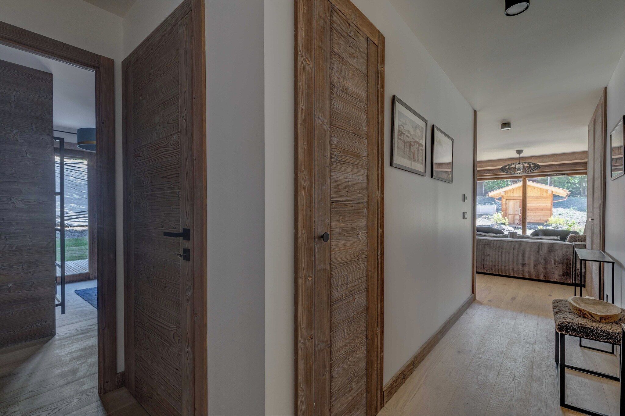 Un couloir avec des portes en bois, un banc et une vue sur un espace détente doté d’une structure en bois.