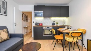 Een ruimtelijk ingerichte leefruimte met een kitchenette, eethoek en een bank.