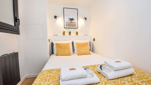 Een hotelkamer met een bed, twee kussens, een lijst met een foto aan de muur en een radiator.
