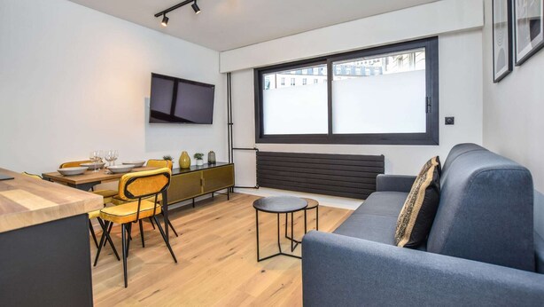 Een moderne woonkamer met een bank, eethoek en een aan de muur bevestigde televisie.