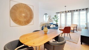 Un salón moderno con una mesa de comedor de madera, sillas grises, un sofá azul y una gran obra de arte abstracta en la pared.