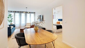 Una sala de estar moderna con una mesa de comedor de madera, sillas negras, un sofá y un televisor.