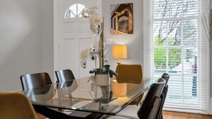 Un coin repas avec une table en verre, des chaises, une plante en pot et un tableau accroché au mur.