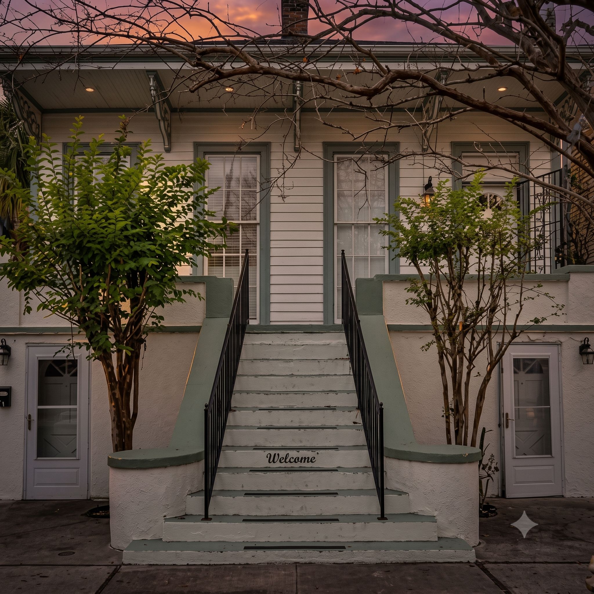 A two-story building with a staircase leading to the entrance, a 'Welcome' sign on the steps, and a tree in front.