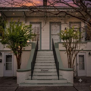 Un bâtiment à deux étages, avec un escalier menant à l’entrée, une pancarte « Bienvenue » sur les marches et un arbre devant.