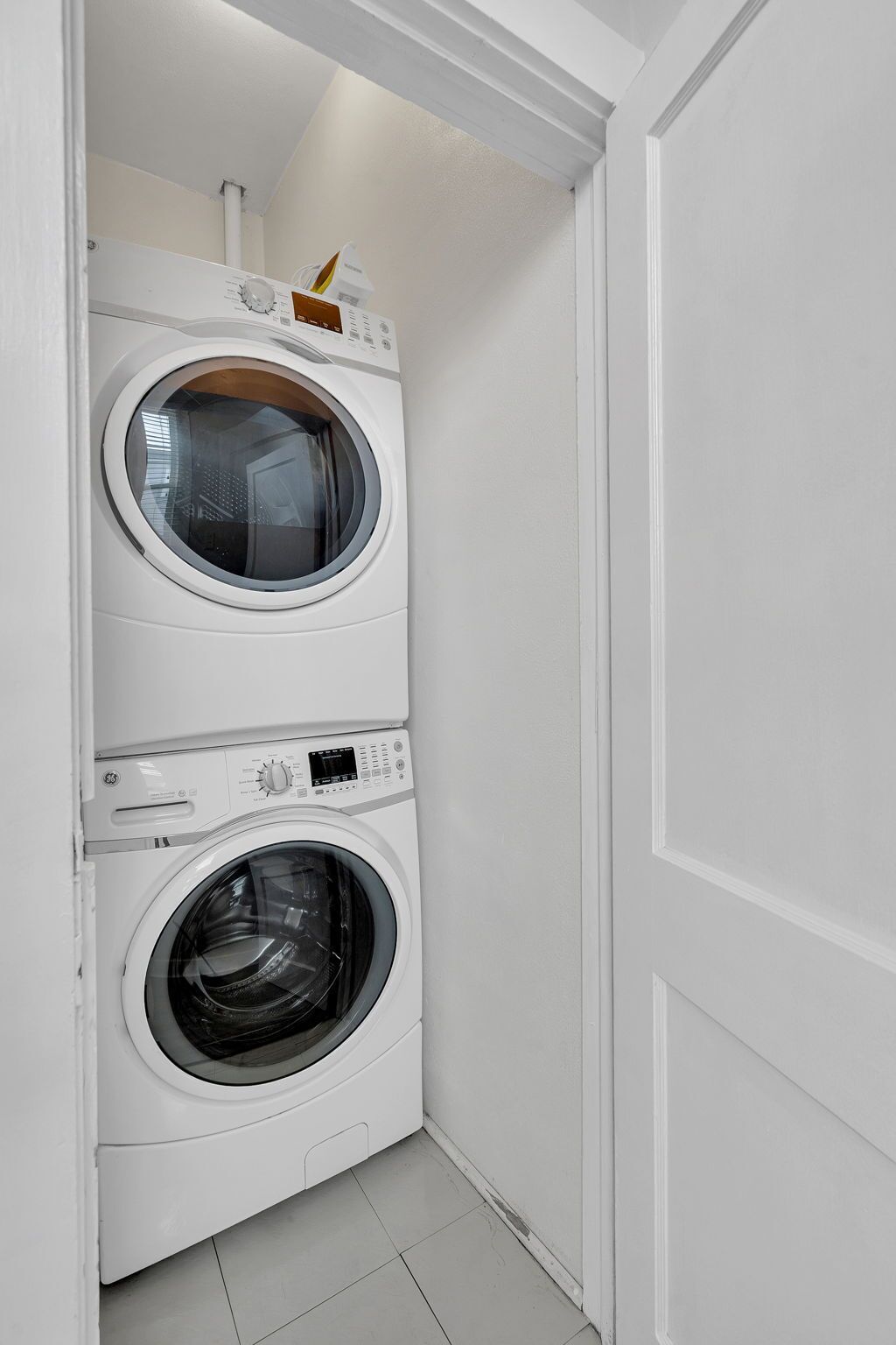 A compact, white laundry room with two stacked front-loading washing machines.