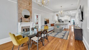 Un salon moderne avec une table à manger en verre, des chaises jaunes, une cheminée et une cuisine en arrière-plan.