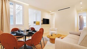 A modern living room with a dining area, a sofa, and a TV mounted on the wall.