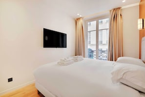 Quarto de hotel com cama, televisão de tela plana na parede e janela com cortinas.