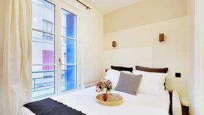 A hotel room with a bed, a bedside table, a window with curtains, and a view of the outside balcony.