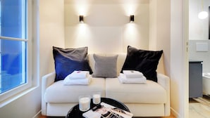 A modern room with a sofa, two wall-mounted lights, a window, and a small table with a magazine and candles.