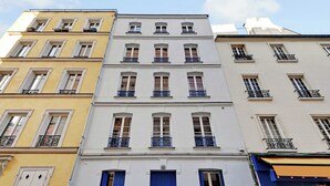 A multi-story building with a central blue door, white and yellow facades, and balconies with black railings.