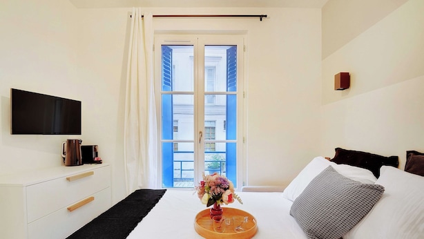 A hotel room with a bed, a flat-screen TV, a coffee maker, and a window with curtains.