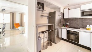 A modern kitchen with a built-in oven, microwave, and stainless steel refrigerator. There is a bar stool and a dining area with a chair.