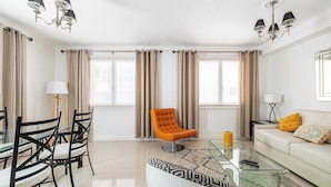 A modern living room with a glass coffee table, a sofa, and a dining area with chairs.