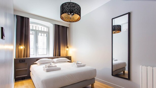 Una habitación de hotel moderna con una cama grande, un espejo y una ventana con cortinas.