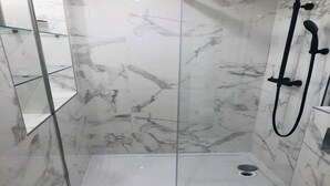 Un baño moderno con paredes de mármol, cabina de ducha de vidrio y un pequeño espacio para el lavamanos.