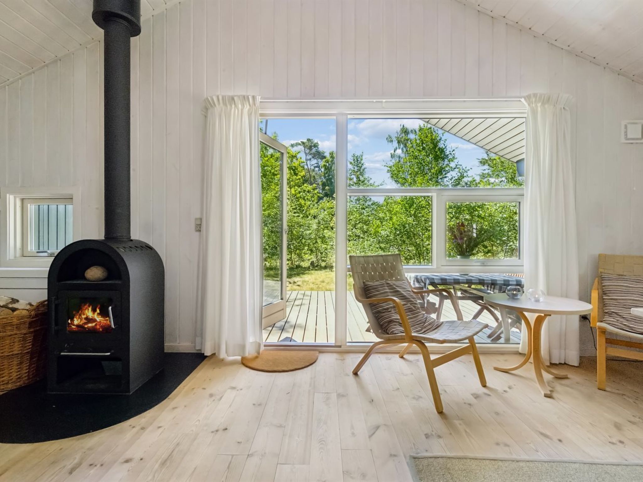 A cozy room with a wood-burning stove, a dining area with chairs, and a large sliding glass door leading to an outdoor deck.