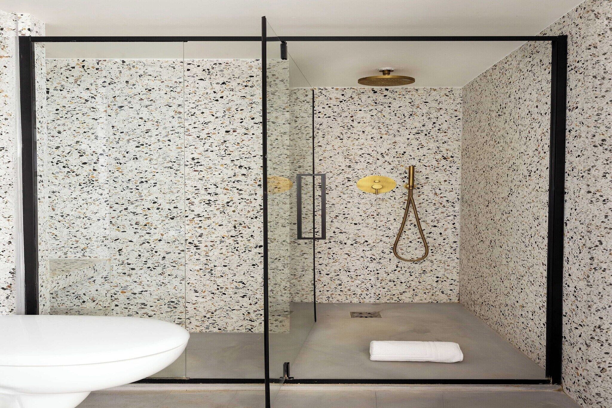 A modern shower with a glass door, a white sink, and a towel on the floor.