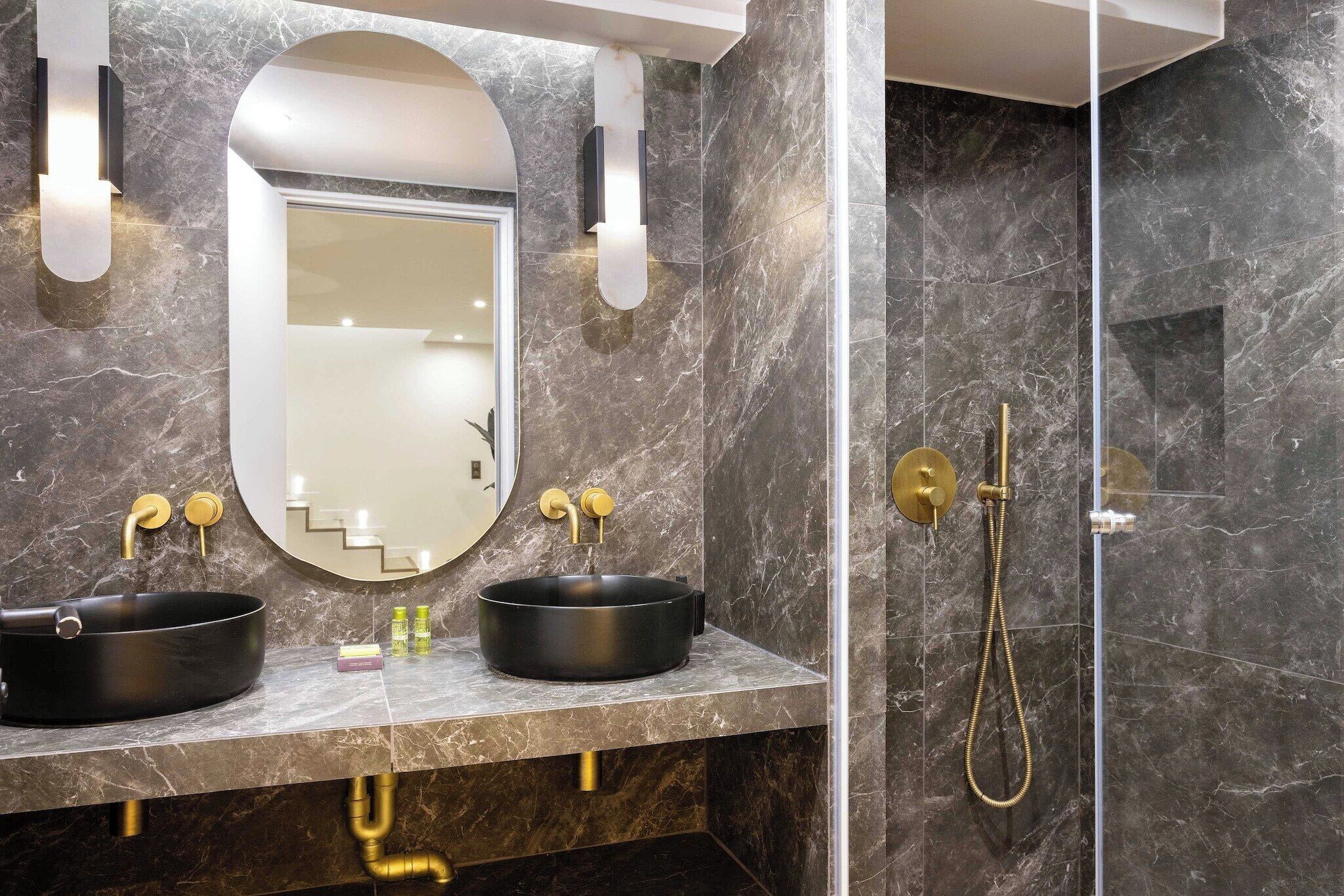 A bathroom with two black sinks, a mirror, and a gold showerhead.