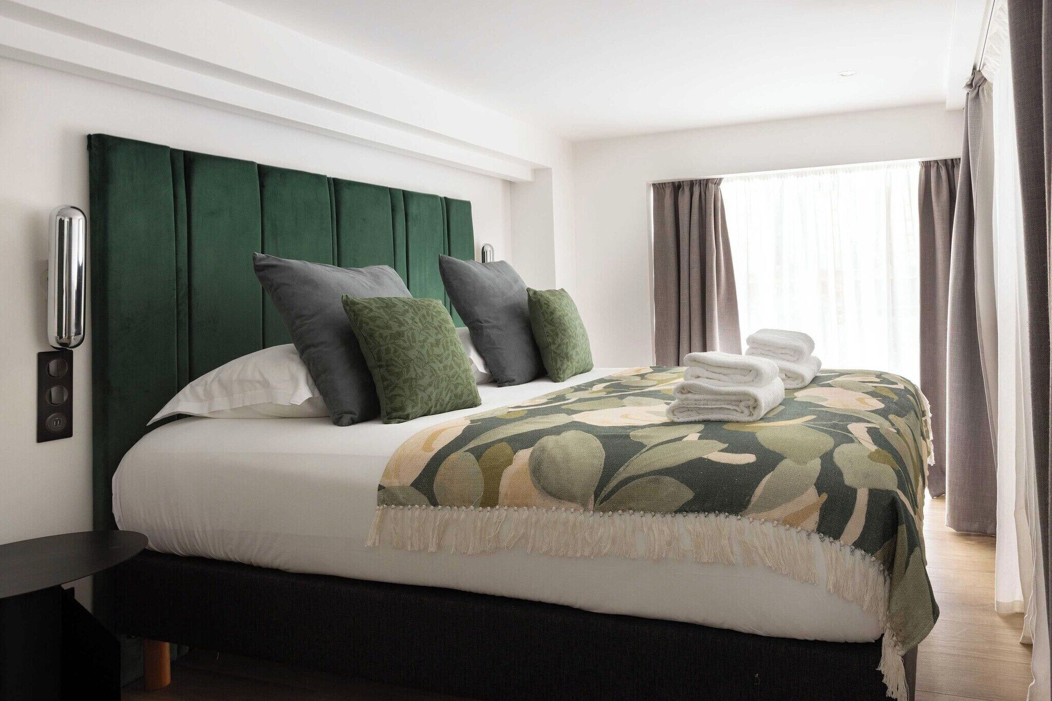 A neatly made bed with a green headboard, white bedding, and a patterned throw blanket.