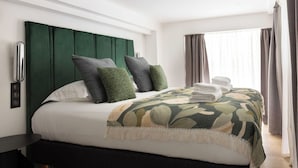 A neatly made bed with a green headboard, white bedding, and a patterned throw blanket.