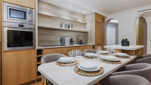 A modern kitchen with built-in appliances, a dining area with a long table set for four, and a small island with a sink and countertop.