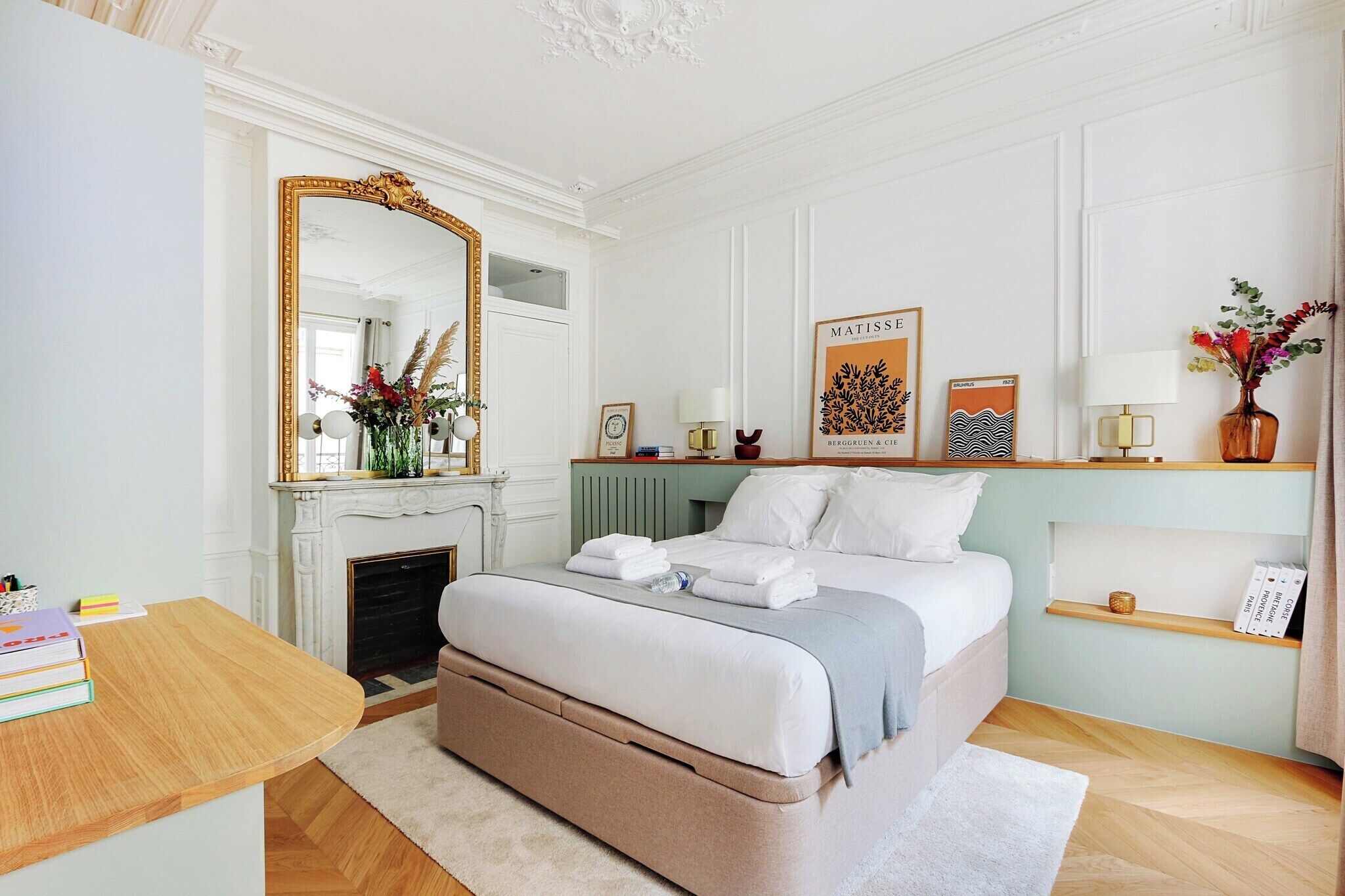 Une chambre avec un grand lit, un miroir, une cheminée et une bibliothèque.