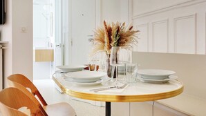 A dining table set with plates, glasses, and cutlery, with a vase of dried flowers in the center.