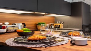 Eine moderne Küche mit dunklen Schränken, einer Holz Arbeitsplatte, einem Toaster, einer Obstschale und einem Croissant auf einem Teller.